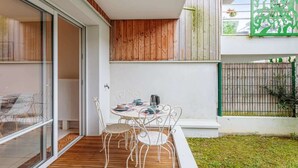 A modern outdoor patio with a wooden deck, a round table with chairs, and a glass door leading to a room. - Beautiful apartment - near the beach (La Rochelle)