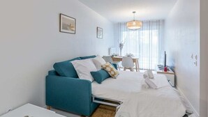 A modern, well-lit bedroom with a teal sofa, a neatly made bed, and a dining area with natural light. - Beautiful apartment - near the beach (La Rochelle)