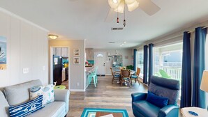 A spacious living room with a sofa, a leather armchair, and a dining area with a table and chairs. A kitchen is visible in the background. - Beach Home With Private Pool & Beach Access- Sleeps 4 (Gulf Shores)