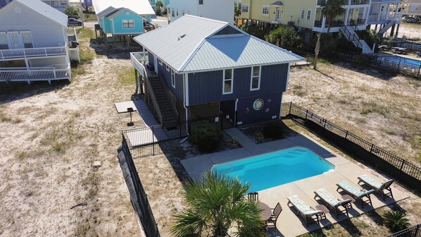 Ein Strandhaus mit Swimmingpool, einer überdachten Terrasse und einem kleinen Garten.