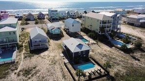 A coastal residential area with multiple two-story houses, a swimming pool, and a beach in the background. - Beach Home With Private Pool & Beach Access- Sleeps 4 (Gulf Shores)