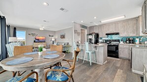 A modern kitchen with grey cabinets, a central island, and a dining area with a round table and wicker chairs. - Beach Home With Private Pool & Beach Access- Sleeps 4 (Gulf Shores)