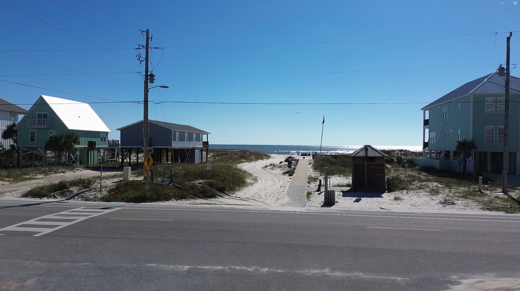 A beachside road with houses, a pedestrian crossing, and a beach in the background.