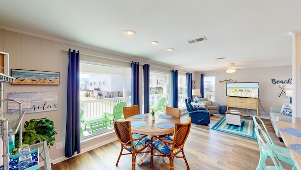A spacious living area with a balcony, a dining table with chairs, and a television. - Beach Home With Private Pool & Beach Access- Sleeps 4 (Gulf Shores)