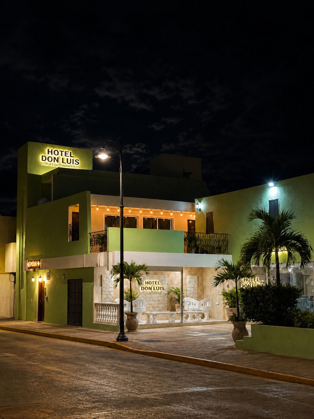 A two-story hotel named 'Hotel Don Luis' with a balcony on the upper floor, a reception area with a glass facade, and a well-lit entrance.