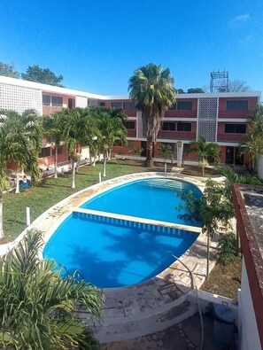 A swimming pool surrounded by palm trees and a building with a red and white facade. - Hotel Don Luis  (Valladolid)