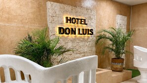 A reception area with a stone wall, a sign reading 'HOTEL DON LUIS,' and two white chairs with a plant in the background. - Hotel Don Luis  (Valladolid)