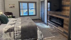Un dormitorio con una cama grande, un televisor montado en la pared y una ventana con vistas a un estacionamiento.