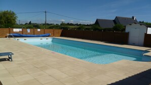 Una piscina rectangular con una solana empedrada, un bote inflable azul y un pequeño cobertizo al fondo.