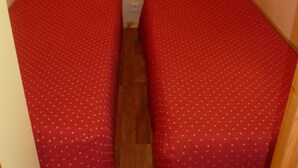 Una habitación pequeña con dos camas, cada una con una colcha roja y suelo de madera.