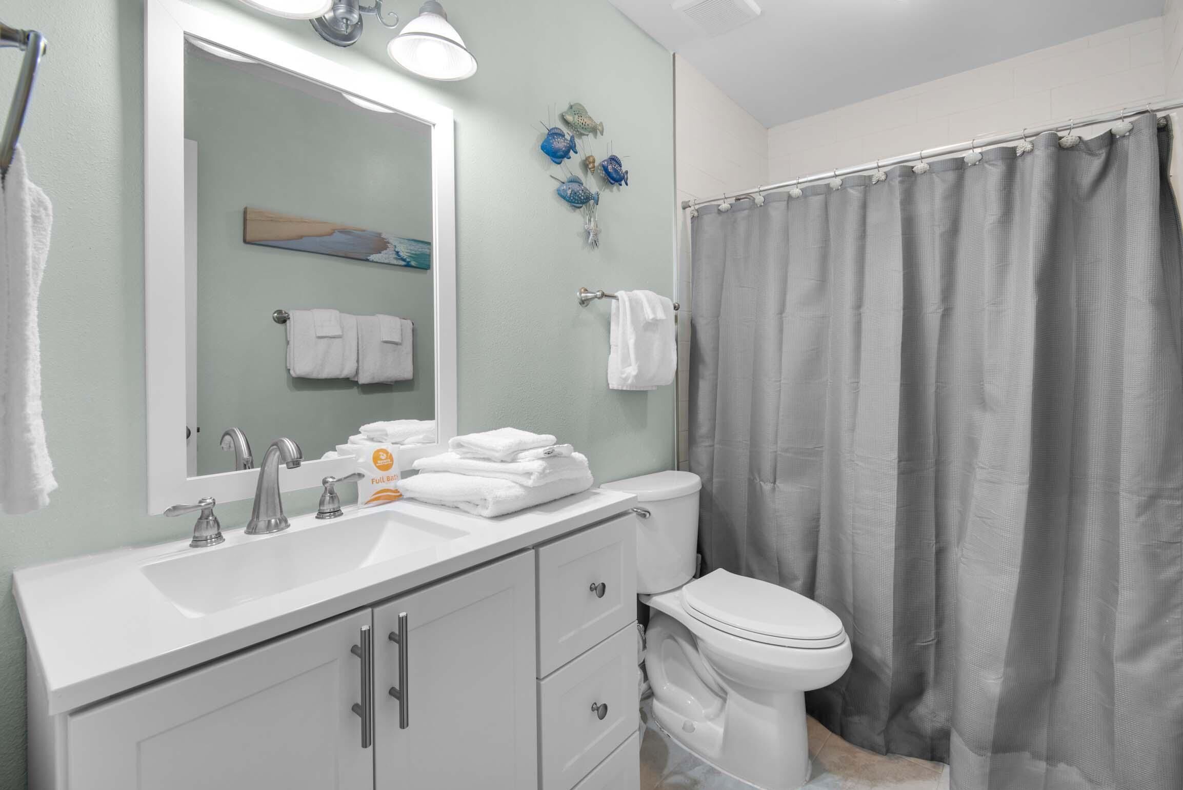 A bathroom with a white sink, a toilet, a shower curtain, and a mirror.
