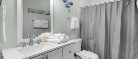 A bathroom with a white sink, a toilet, a shower curtain, and a mirror.
