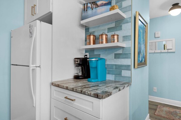 Eine Küche mit einem weißen Kühlschrank, einer Kaffeemaschine und Kupferkochtöpfen auf einem blauen Regal.