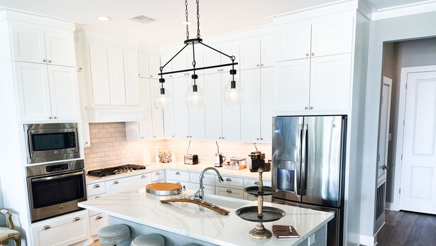 A modern kitchen with white cabinetry, stainless steel appliances, a large island with stools, and a pendant light fixture. - Beautiful decorated family home on the beach (Galveston)