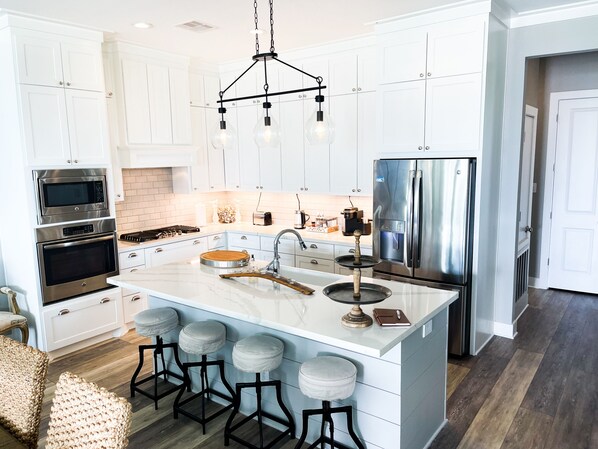 A modern kitchen with white cabinetry, stainless steel appliances, a large island with stools, and a pendant light fixture.