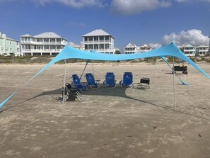 A beach with a blue canopy and beach chairs.