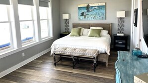 A bedroom with a bed, bedside lamps, a ceiling fan, a window with blinds, and a wall-mounted artwork. - Beautiful decorated family home on the beach (Galveston)