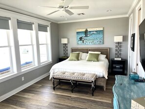 A bedroom with a bed, bedside lamps, a ceiling fan, a window with blinds, and a wall-mounted artwork.