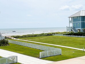A coastal view with a blue building, a white picket fence, and a pathway leading to the beach.