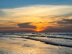 Un coucher de soleil sur une plage, avec des vagues et un ciel dégagé.