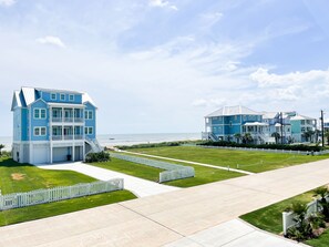 A coastal property with a large blue house featuring a balcony and a spacious lawn.