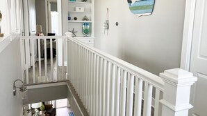 A staircase with white railings leading to a landing with a shelf unit containing decorative items. - Beautiful decorated family home on the beach (Galveston)