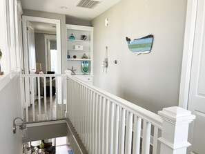 Un escalier avec des rampes blanches menant à un palier où se trouve une étagère contenant des objets décoratifs.