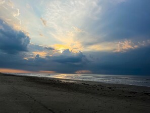 A beach with a wide sandy shore and a view of the ocean under a cloudy sky.