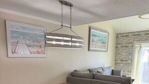A living room with a wooden dining table, a gray sofa, and artwork on the walls.