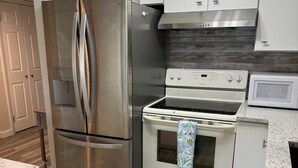 A modern kitchen with stainless steel appliances, white cabinetry, and a wooden floor.