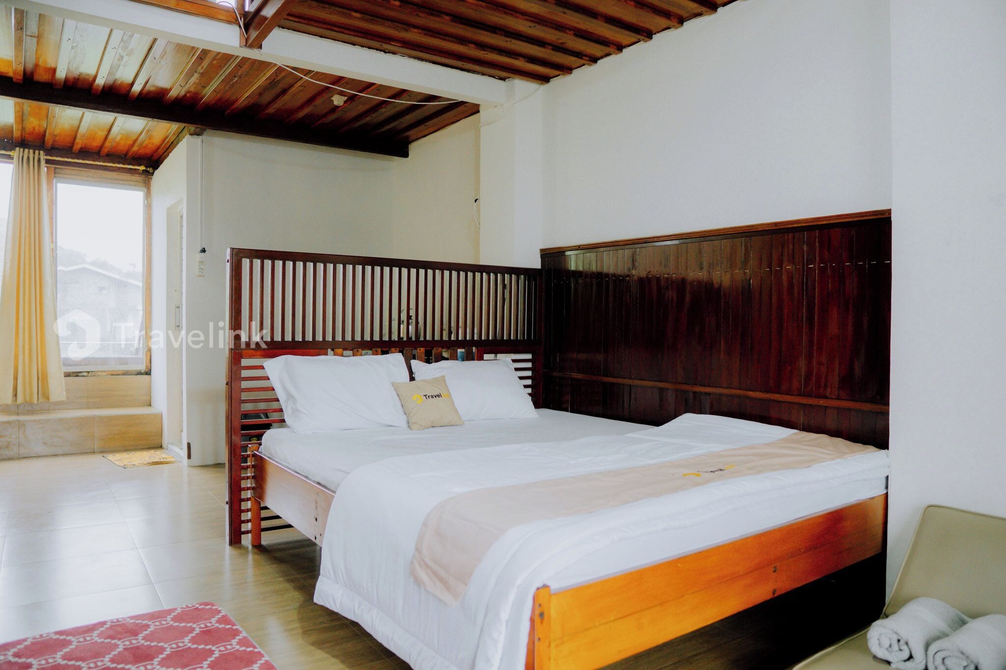Una cama doble bien hecha con cabecera de madera, una mesita de noche pequeña y una toalla enrollada en el suelo.