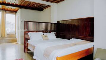 Una cama doble bien hecha con cabecera de madera, una mesita de noche pequeña y una toalla enrollada en el suelo.