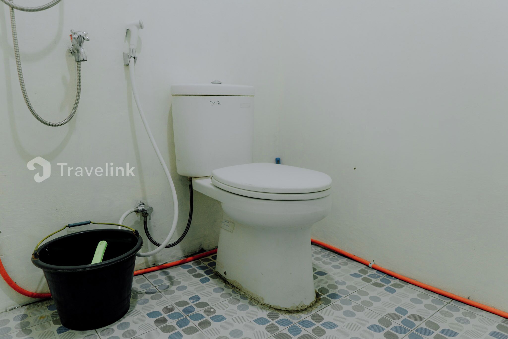 Pieni, yksinkertainen kylpyhuone, jossa on wc, ämpäri ja letku.