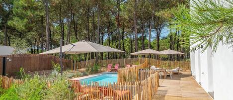 Ein Poolbereich mit Holzterrasse, Liegestühlen und Sonnenschirmen.