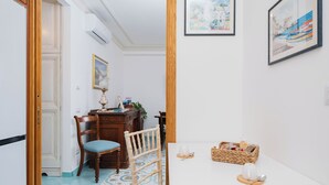 A dining area with a white table, wooden chairs, a wicker basket, and a framed painting on the wall.