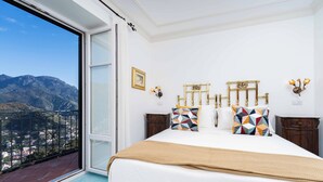 A bedroom with a large bed, a view of mountains, and a balcony with a railing.