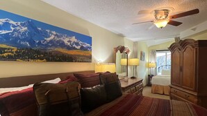 A hotel room with a large bed, a ceiling fan, a painting of mountains, and a view of the room. - Vail Run 4 Bed room Spring Break Week with Heated Pool, Hot Tub, Sauna (Vail)