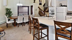 A modern kitchen with a central island, wooden chairs, a dining table, and a staircase leading to a loft. - Vail Run 4 Bed room Spring Break Week with Heated Pool, Hot Tub, Sauna (Vail)