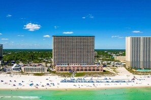 Een hotel aan het strand met meerdere hoge gebouwen, een zandstrand en helderblauwe lucht.