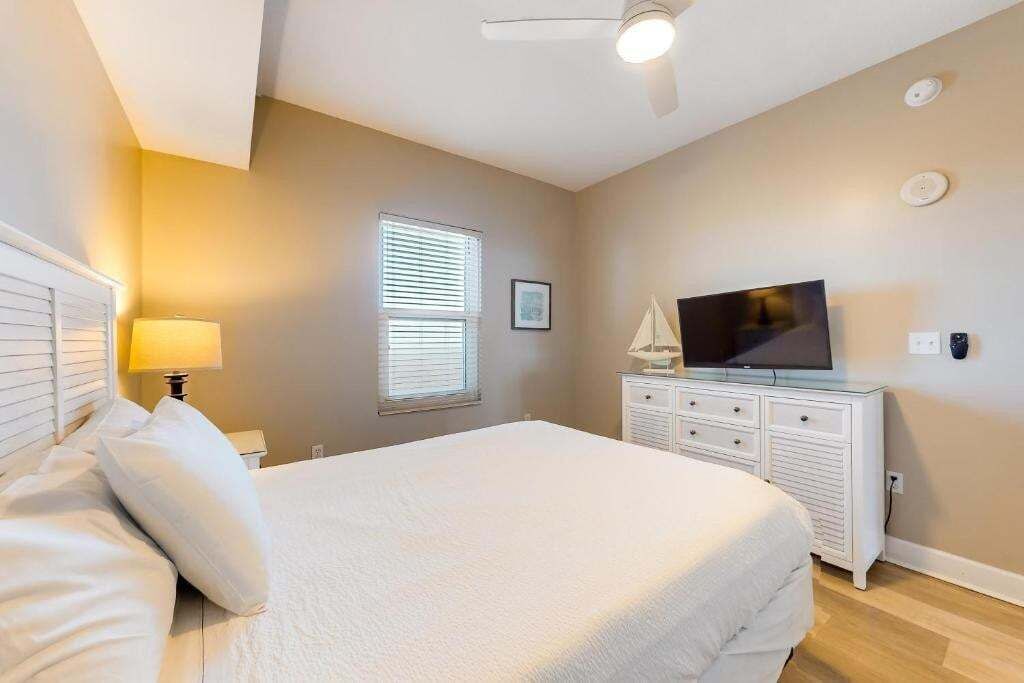 A bedroom with a bed, a TV on a dresser, a ceiling fan, and a window with blinds.