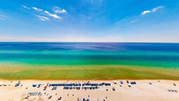 Une plage bordée de rangées de chaises longues et de parasols, un ciel dégagé et une mer calme.