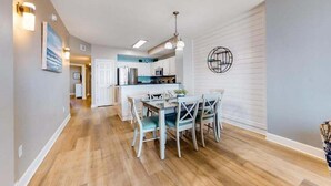 Une cuisine moderne avec des meubles blancs, un coin repas avec une table et des chaises en bois, et un couloir agrémenté de luminaires.