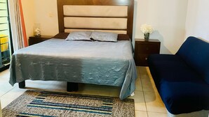 Een keurig opgemaakt slaapkamer met een bed, nachtkastjes, een stoel en een vloerkleed.