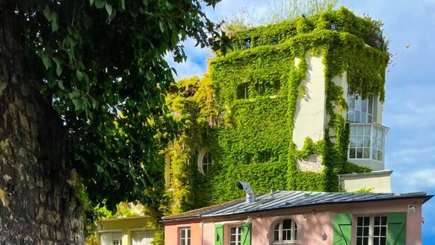 Un restaurant doté d’une terrasse, d’un mur en pierre et d’un bâtiment recouvert de verdure.