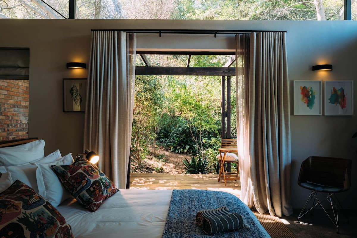 A bedroom with a large bed, a wooden bench, and a view of a garden.