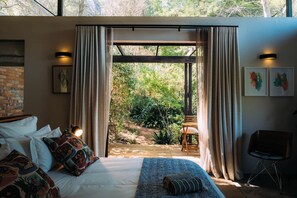 A bedroom with a large bed, a wooden bench, and a view of a garden. - Phakalane Retreat (Cape Town)