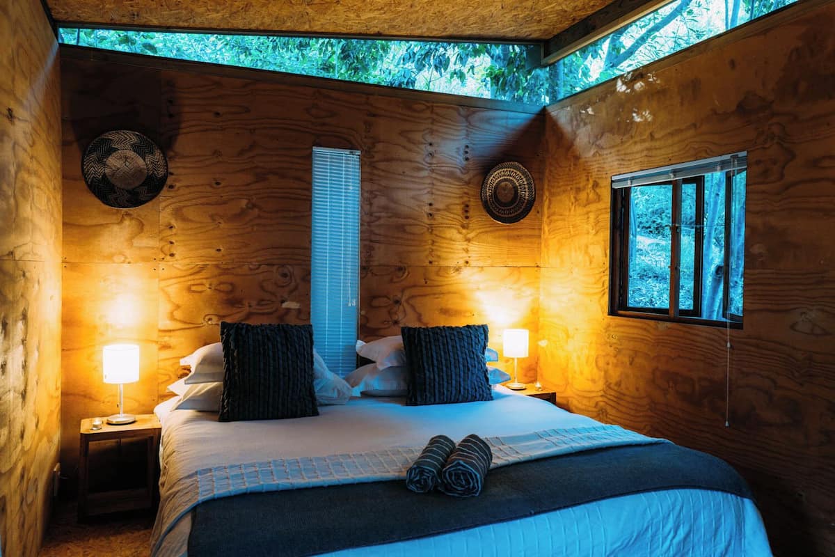 A wooden cabin bedroom with a bed, two nightstands, a window, and a skylight.
