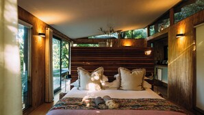 A modern bedroom with a large bed, wooden walls, and a view of greenery outside. - Phakalane Retreat (Cape Town)