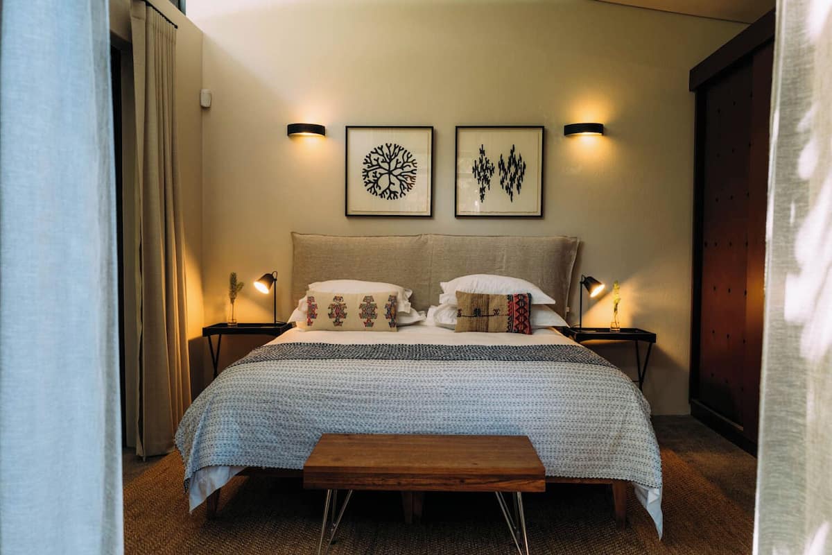 A bedroom with a large bed, two wall-mounted lamps, and two framed artworks.