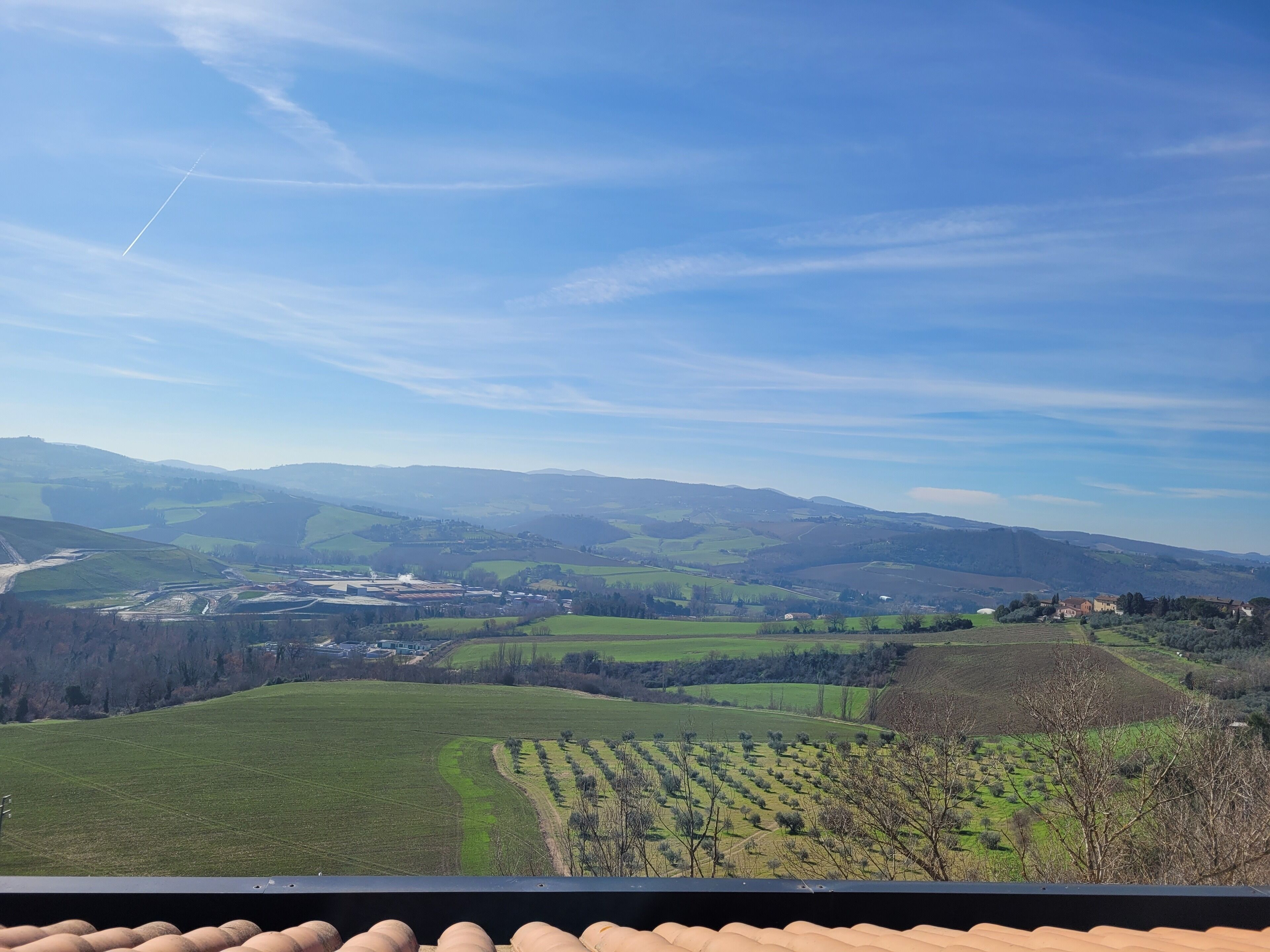 Ein Panoramablick auf eine ländliche Landschaft mit sanften Hügeln, Feldern und einer in der Ferne liegenden Stadt.